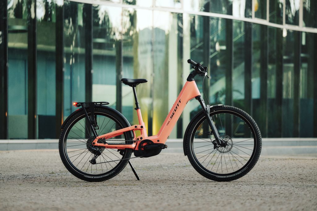 SCOTT E-Ville 10 SUV in Peach Pink vor einer Glasfassade – Foto: © Scott Sports / Paul Masukowitz